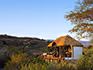 A thatched chalet surrounded by nature with rocky mountains in the background. 