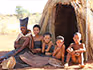 A family of Khoi San bushmen sitting in front of a traditional bushman hut. 