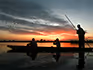 A silhouette of two people on a mokoro taking pictures at sunset while being poled along the river. 