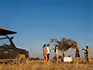 A Ongava safari vehicle parked at a sundowner spot in the bush where four guests are chatting with their guide. 