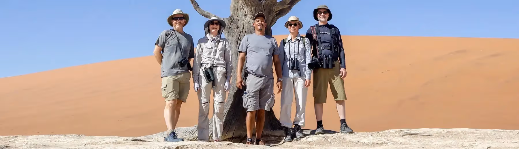Four guests posing with their private guide for a photograph at a petrified tree in Sossusvlei.