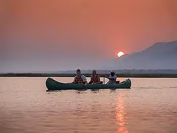Three people on a canoe at sunset on the river.