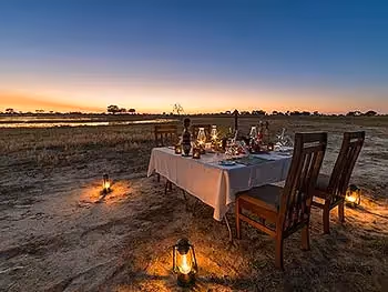 An outdoor dining table set for four on a sandy patch next to a river. 