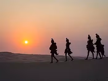 The silhouette of four Himba ladies and a child walking on a sand dune at sunset.