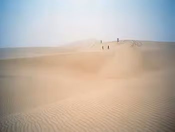 A distant view of people walking and playing on a sand dune in the fog. 