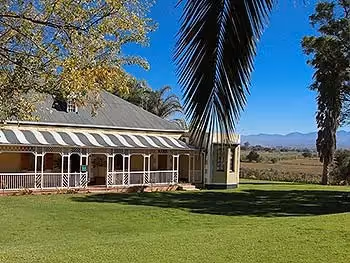 View from the lawn onto a lodge building and patio with mountains in the distance. 
