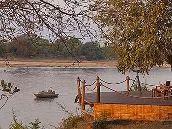 A view through the trees of a lodge deck overlooking a boat passing by on the river.