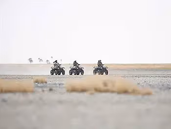Three people on a quad bike excursion on an open pan.