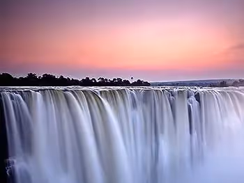 Victoria Falls at sunrise with a pink sky.