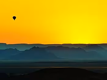 The silhouette of a hot air balloon in the distance above a desert landscape at sunrise.