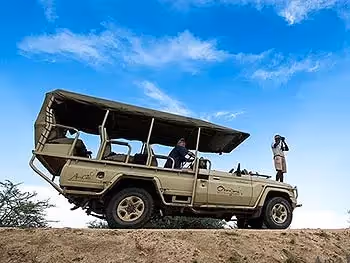 An open safari vehicle at Okonjima with a guest and a guide on the bonnet looking with binoculars. 