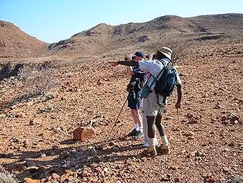 A guide showing something to two guests looking through binoculars at something in the distance. 