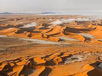 An aerial view from above scattered clouds over the endless sand dunes of the Namib Desert.