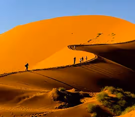 Adventurous travellers climb a towering sand dune in Sossusvlei, Namibia.