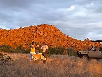 A guide and a guest enjoying a sun downer in the bush against a granite boulder outcrop. 