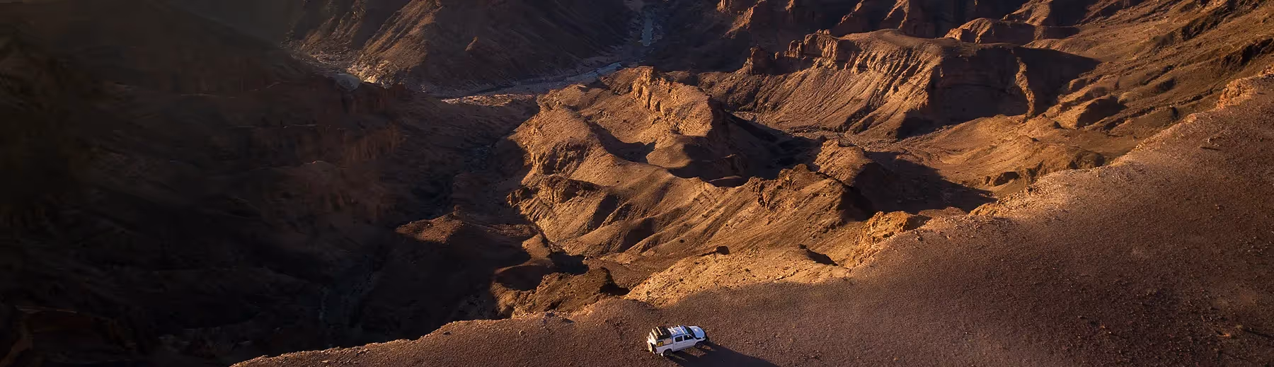 Breathtaking perspective: Aerial view of a safari car navigating the rugged terrain alongside the majestic Fish River Canyon, capturing the vastness and beauty of this natural wonder from above.