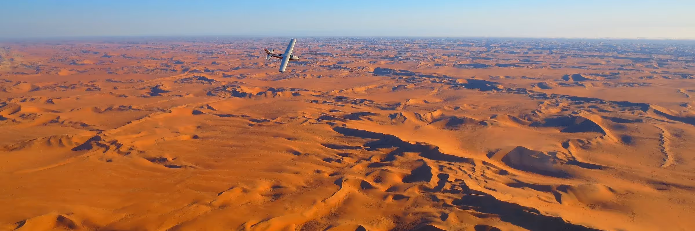 Luftaufnahme eines kleinen Flugzeugs, das über die majestätischen Dünen von Sossusvlei gleitet und die atemberaubende Wüstenlandschaft Namibias zeigt.