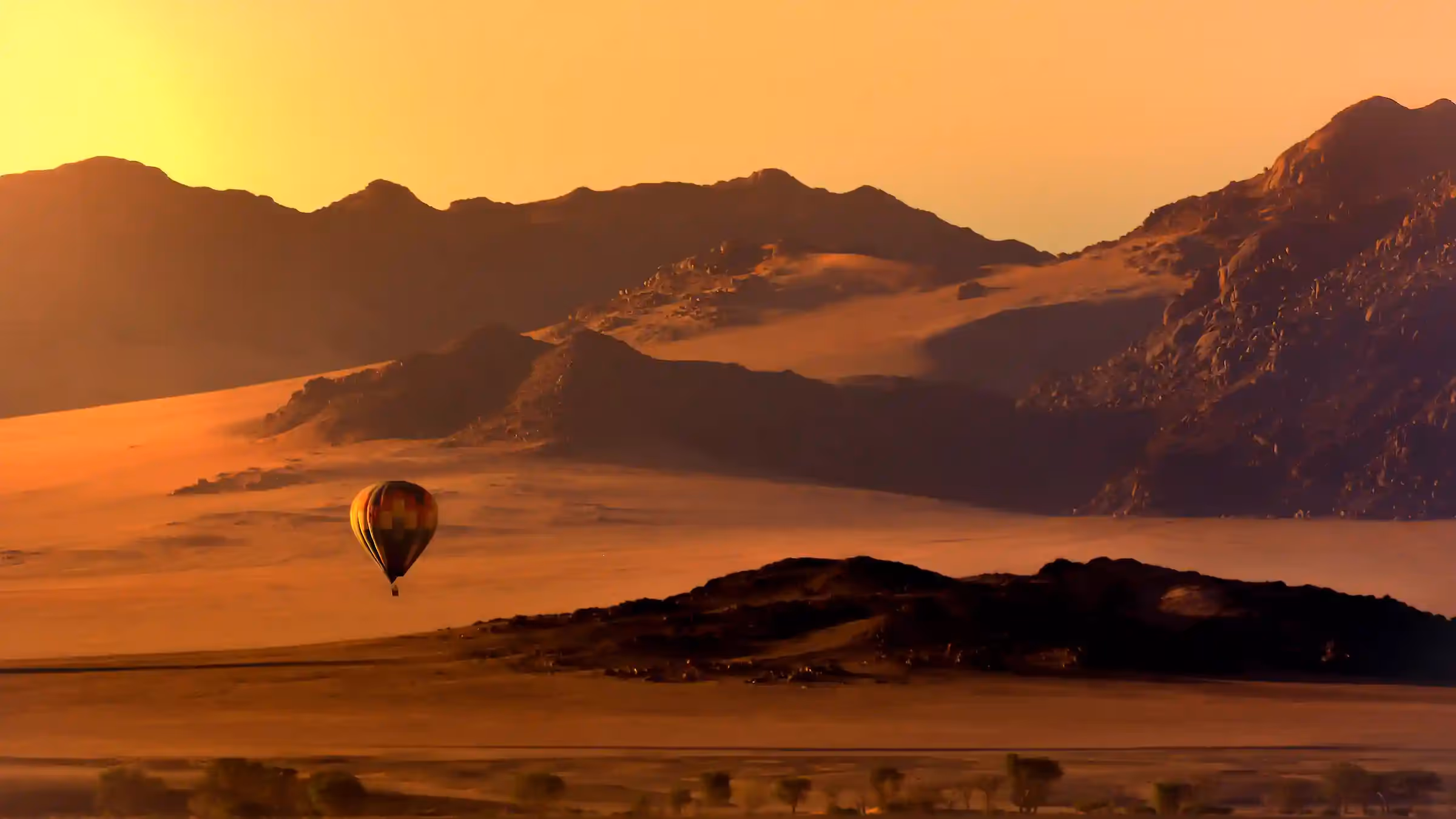 Hot air balloon floats peacefully over the stunning landscape of Sossusvlei at sunrise.