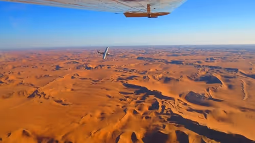 Aerial view of a small airplane gliding over the majestic Sossusvlei dunes, showcasing the stunning desert landscape of Namibia.