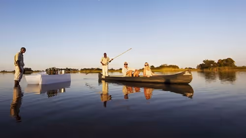 Guests enjoy a serene mokoro ride with sundowner drinks set up in the tranquil waters of Okavango Delta.