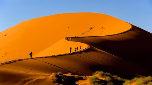 Adventurous travellers climb a towering sand dune in Sossusvlei, Namibia.