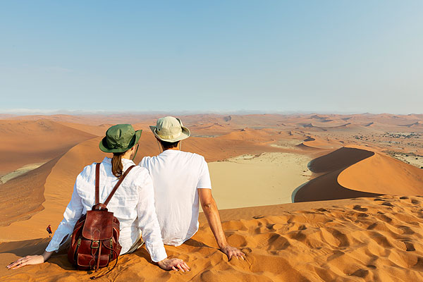 A couple sit in the sand overlooking the sand dunes in Sossusvlei