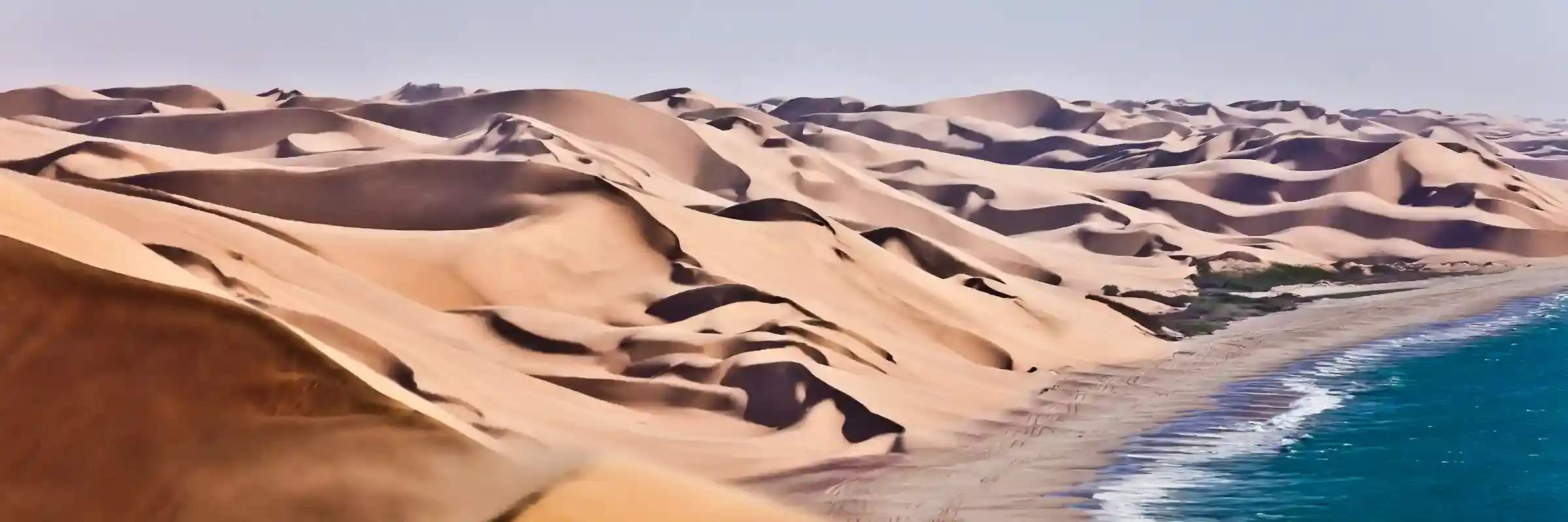 Panoramablick auf die Stelle, an der die hoch aufragenden Sanddünen auf den Ozean an der Skelettküste Namibias treffen. 