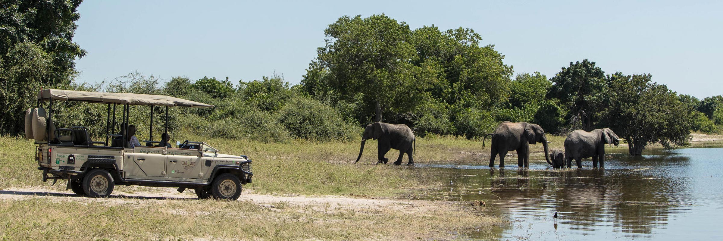 Safari-Teilnehmer beobachten Elefanten im Wasser während einer Pirschfahrt im Chobe-Nationalpark.