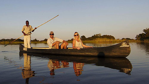 Guests enjoy a serene mokoro ride with sundowner drinks set up in the tranquil waters of Okavango Delta.