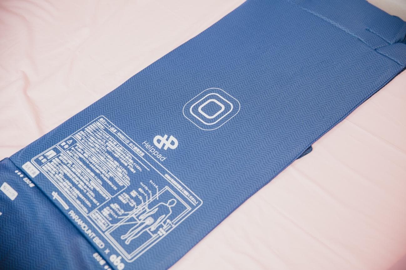 企業間の壁はあろうともワンチームとして動いていく。その姿勢を表すエピソードがある。 Helppad は開発段階で別の製品名を付けられていたが、流通を前に「Heplpad」へと改められた。変更理由はロゴを刷新するためだ。Helppad のロゴはアルファベットの「H」を斜めに傾けたデザインで、線の角度はパラマウントベッド社のロゴマークに合わせてある。つまり、2社で力を合わせてプロジェクトを進めることを表現している。