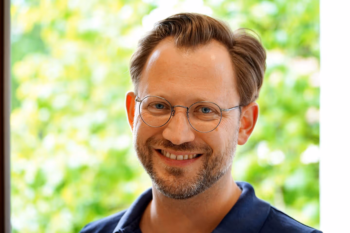 Portrait Prof. Dr. med. Ulrich Straßen, mit runder Brille und Bart, lächelnd vor unscharfem grünen Hintergrund