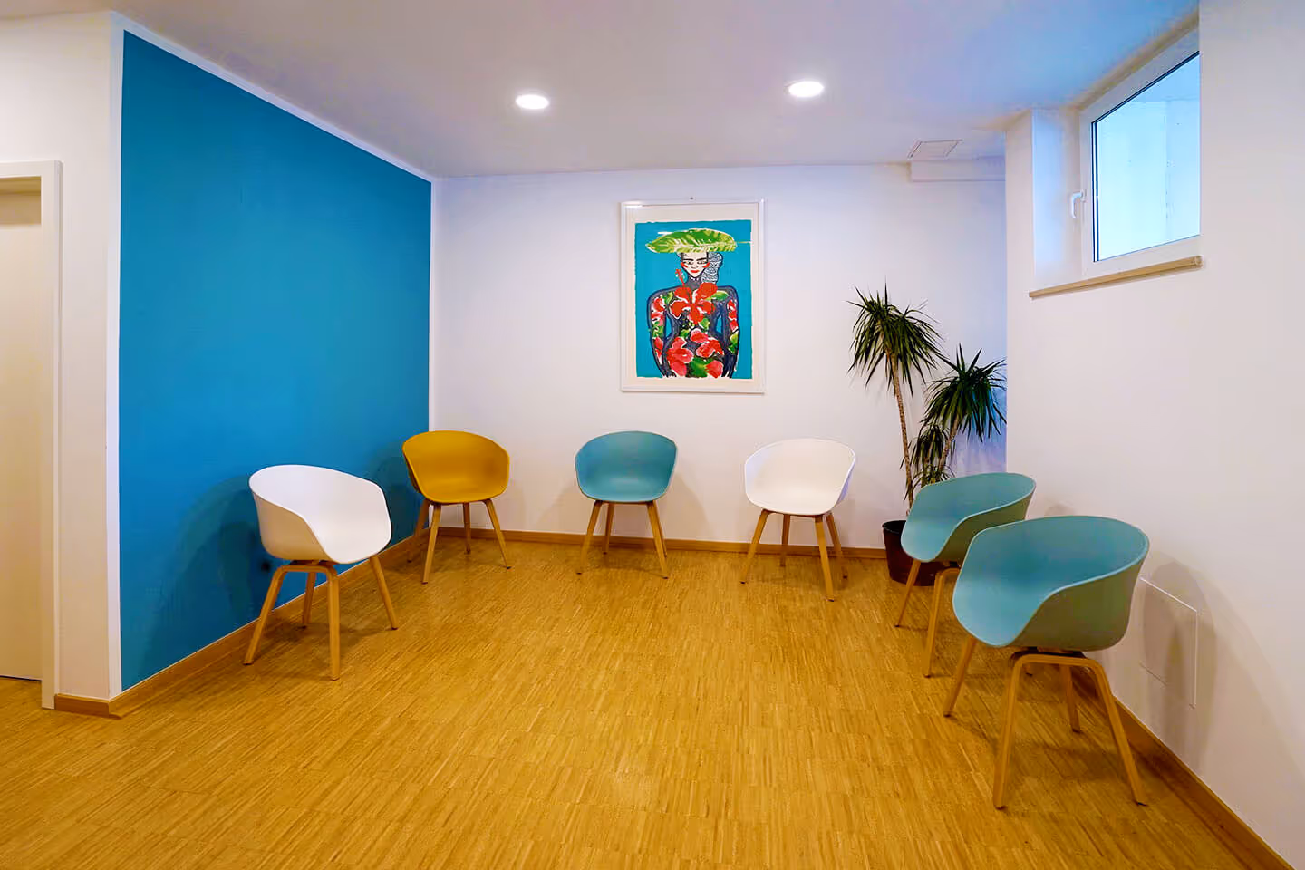 Foto vom hellen, modernen, freundlichen Wartezimmer mit bunten Stühlen und einem schönen Gemälde an der Wand