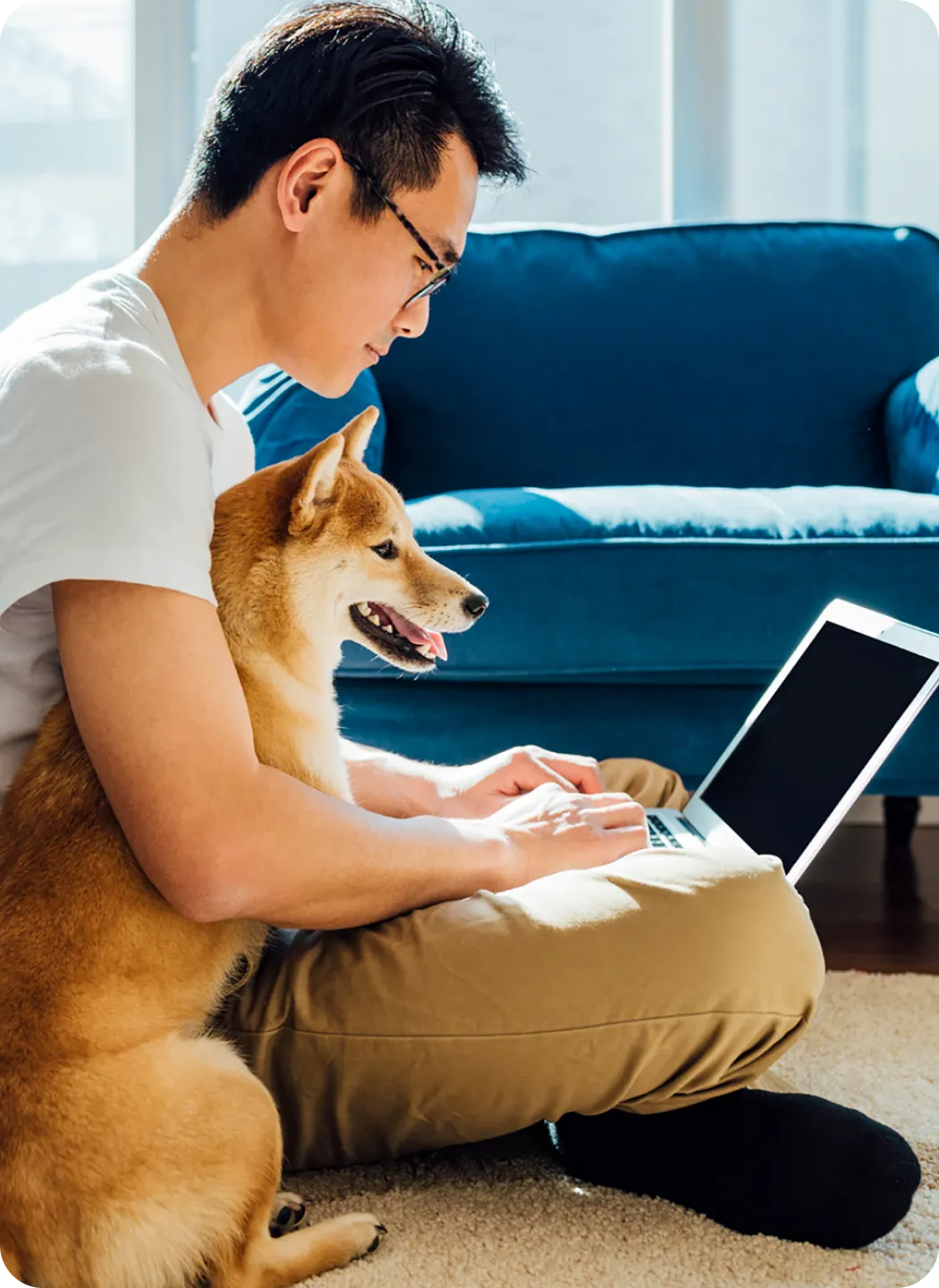 Person sitting on the ground using a laptop, with a dog resting beside them