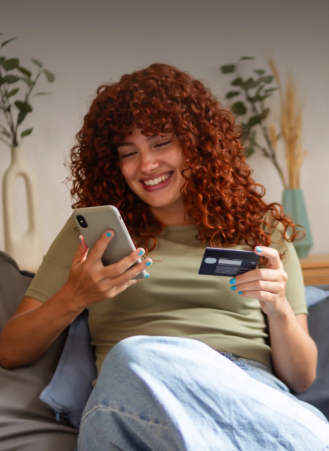Woman smiling while looking at her phone and holding a credit card