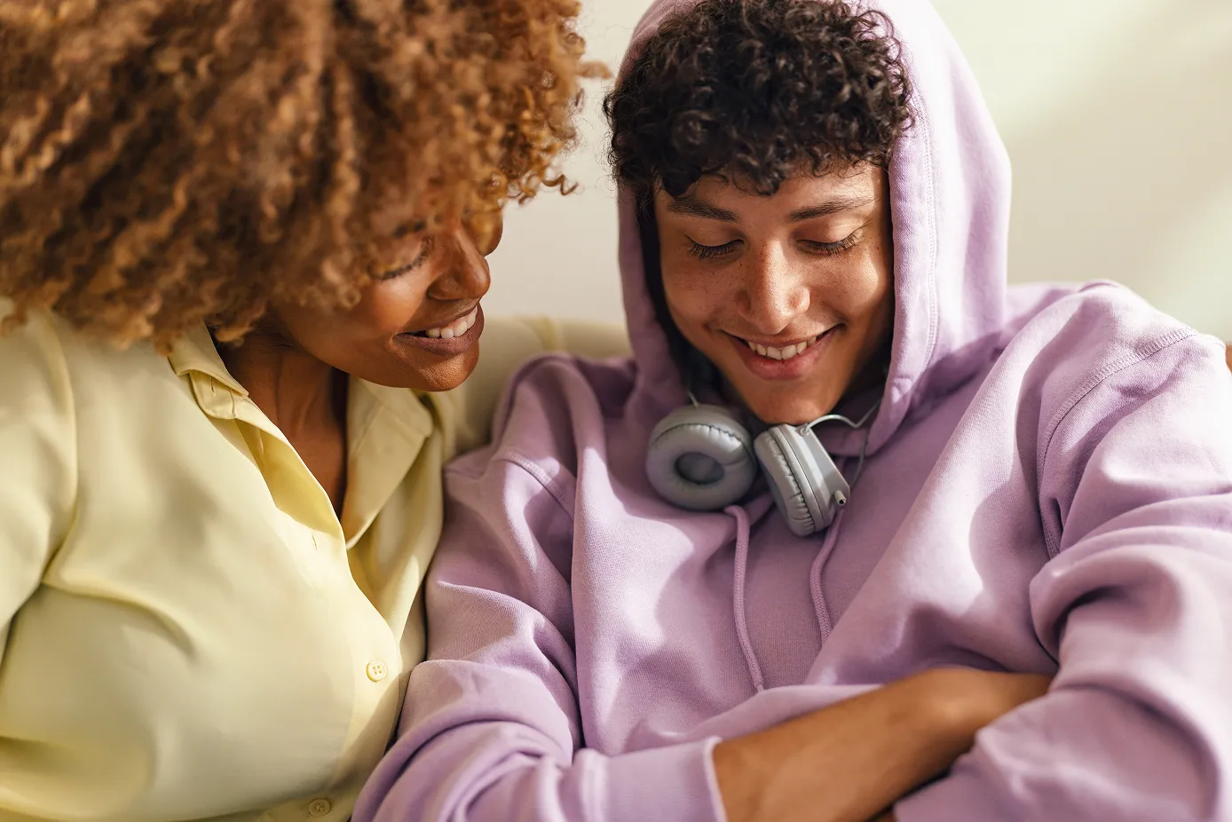 Mother and child wearing headphones, looking down and smiling together