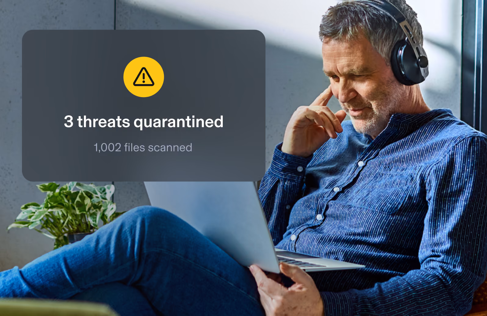 Aura widget showing 3 threats quarantined and 1,002 files scanned overlayed on top of an image with a man browsing the internet on his laptop.