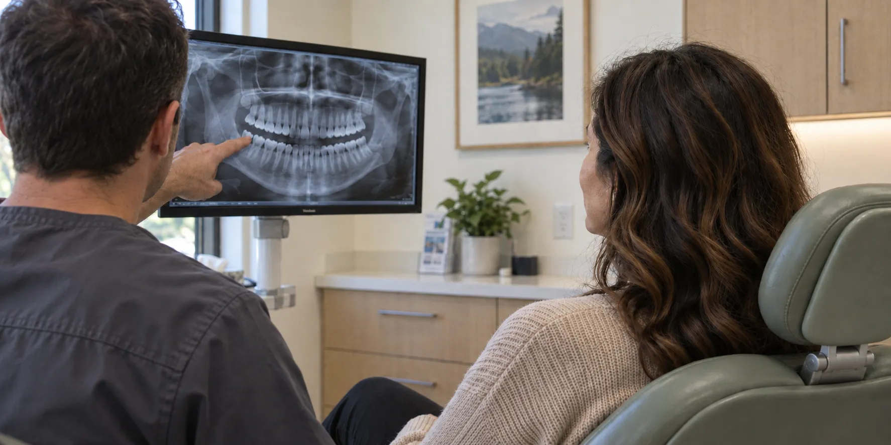 Over-the-shoulder view of a patient and clinician reviewing a dental X-ray