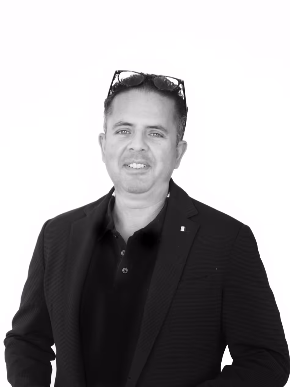 Man med mörkt hår och glasögon på huvudet, klädd i svart kavaj och svart pikétröja, ler mot kameran.