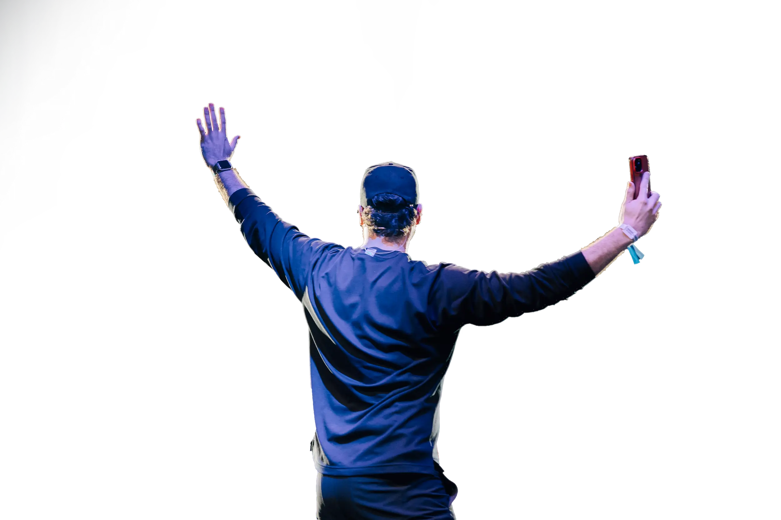 Man wearing a cap with arms raised, holding a smartphone in one hand, viewed from behind.