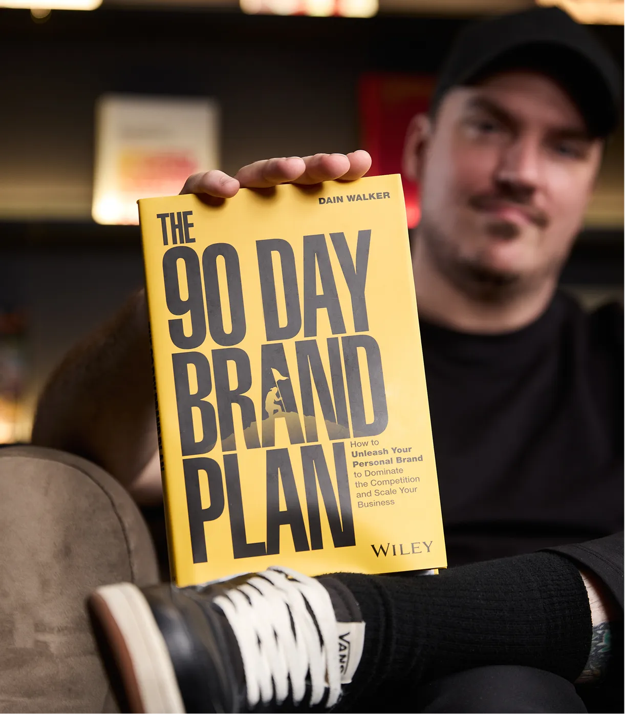 Person holding the yellow book 'The 90 Day Brand Plan' by Dain Walker, published by Wiley.