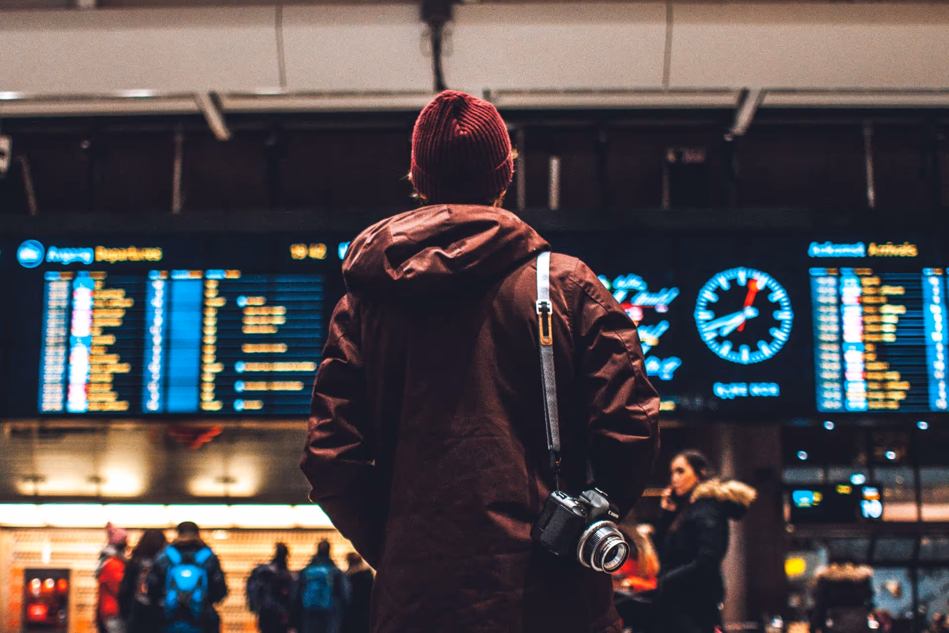 Un homme, vu de dos, portant une caméra sur son épaule à l'aéroport.