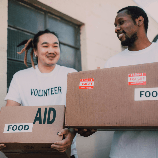 Two volunteers carrying aid boxes labeled food, showing community support and charity efforts.