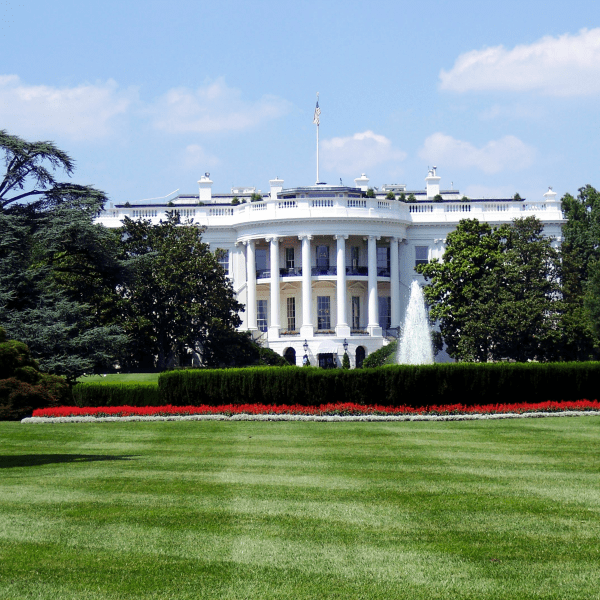 Iconic view of the White House with lush gardens and a central fountain on a sunny day.