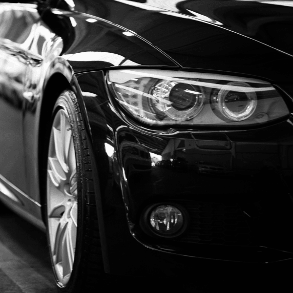 Close-up black and white image of a luxury car line-up focusing on vehicle headlights.