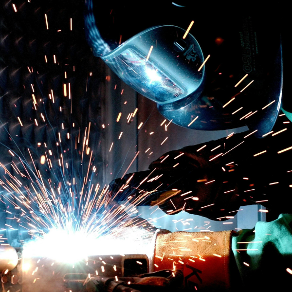 A focused welder works with metal in an industrial setting, creating vibrant sparks.