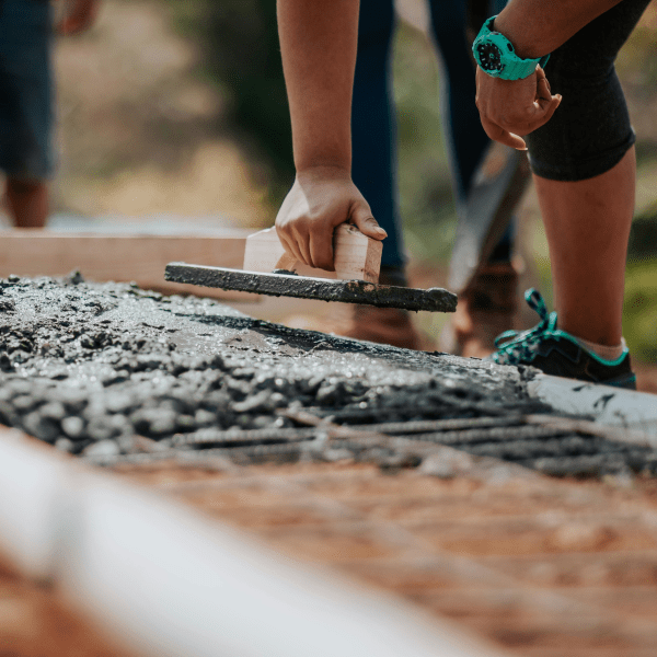 Construction workers leveling fresh cement on a sunny day at an outdoor site.