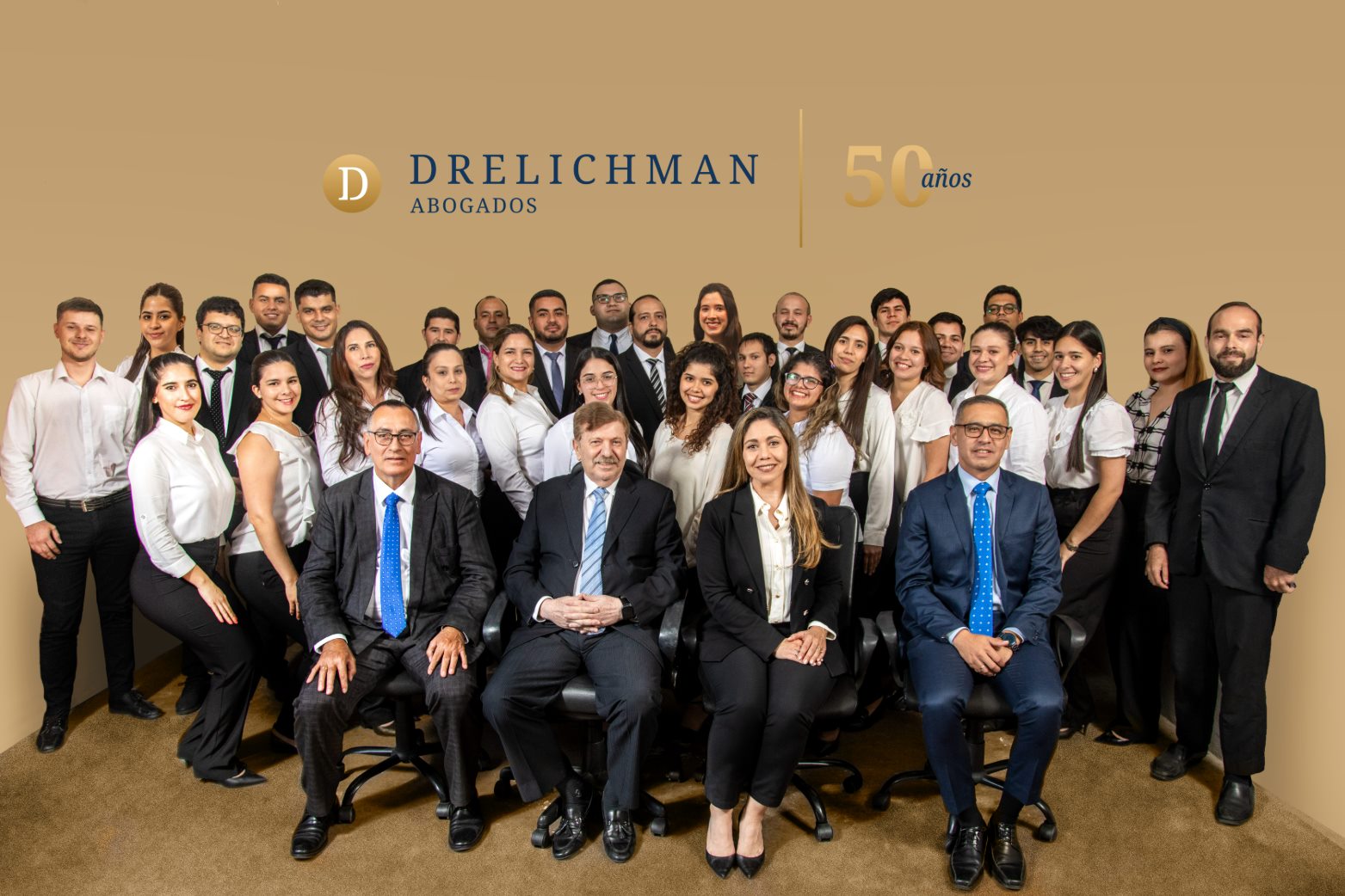 Equipo completo de Drelichman Abogados en la sala de reuniones: los cuatro abogados seniors sentados en la primera fila y el resto del equipo de pie detrás. En la pared del fondo, el logotipo del estudio y la leyenda 50 años.