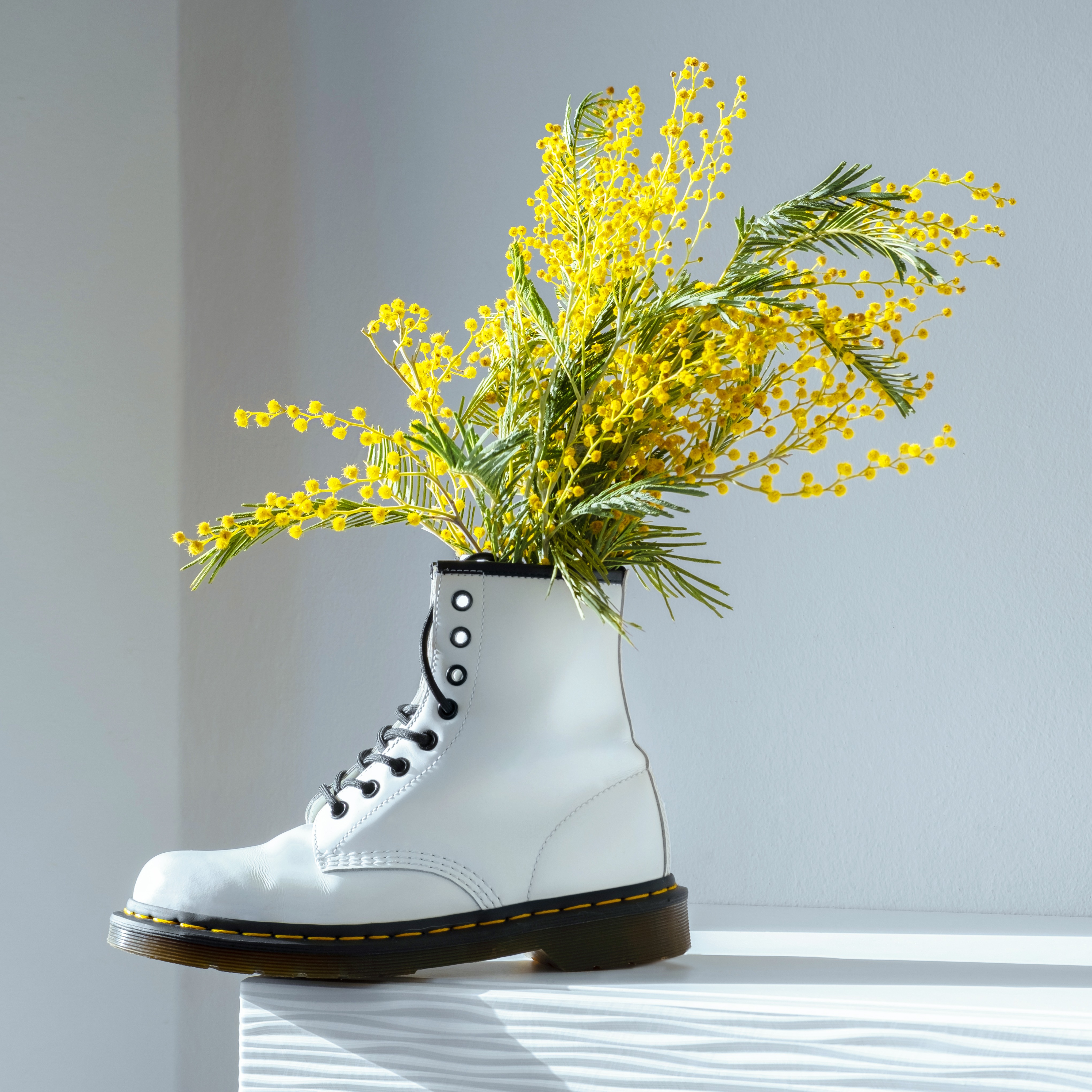 A white Doc Marten boot holding a bouquet of yellow flowers