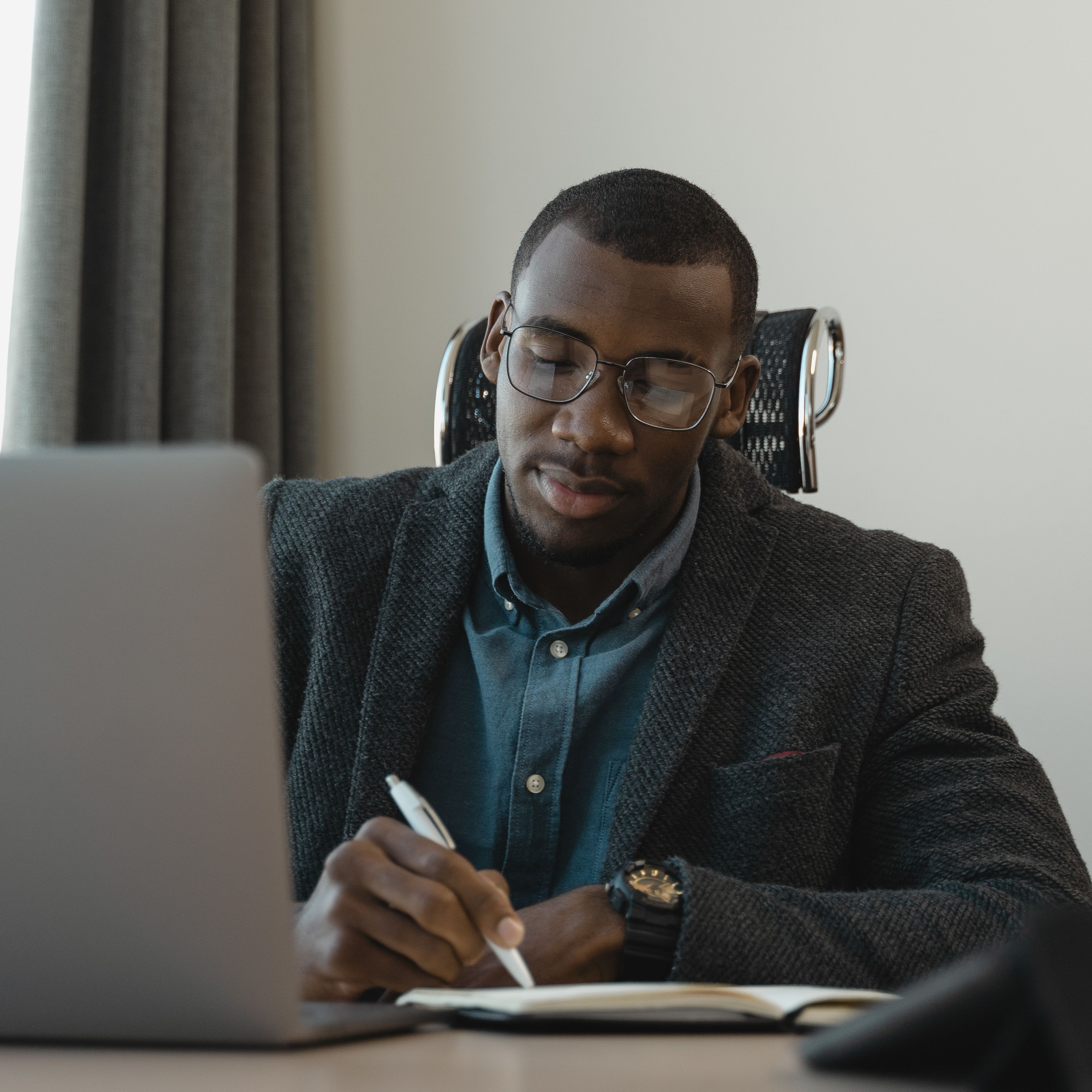 A man sitting in front of a computer, taking notes on a notepad.
