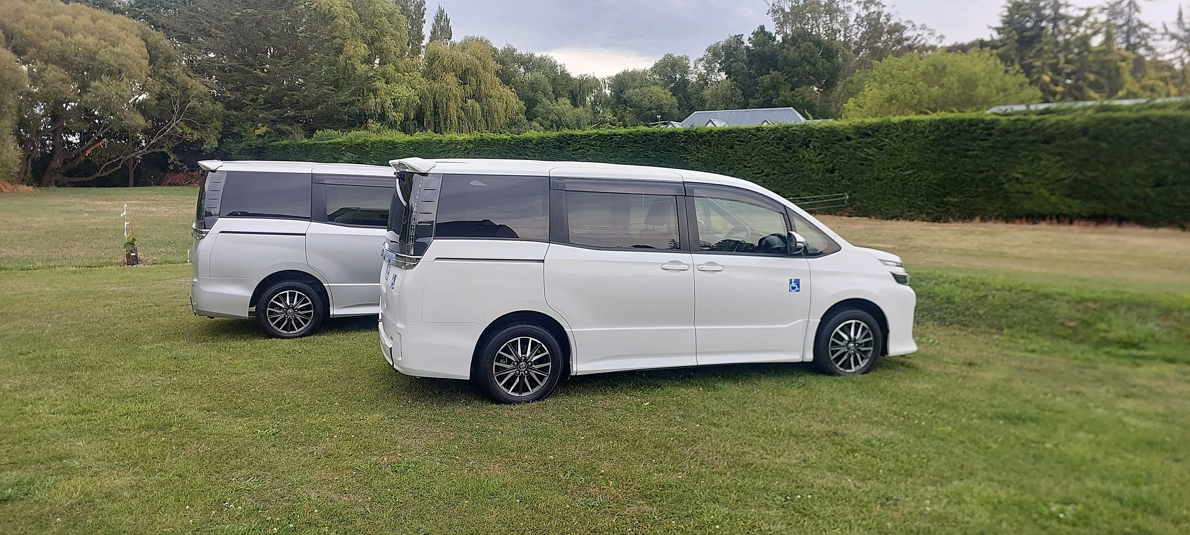 Two white minivans parked on a field.